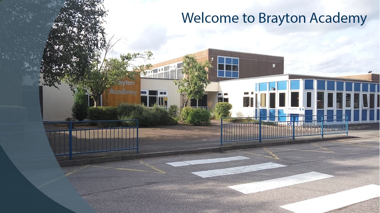Welcome sign at Brayton Academy, featuring a modern building with greenery and a blue fence in front.