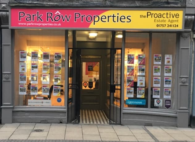 Shopfront of Park Row Properties with bright signage, window displays featuring property listings, and tiled entrance.