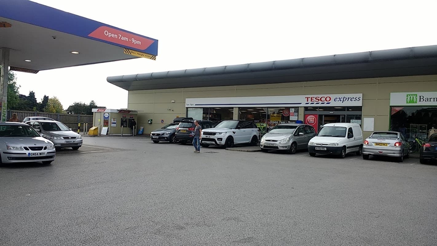 Tesco Express petrol station with parked cars and a customer walking towards the entrance in Brayton, North Yorkshire.