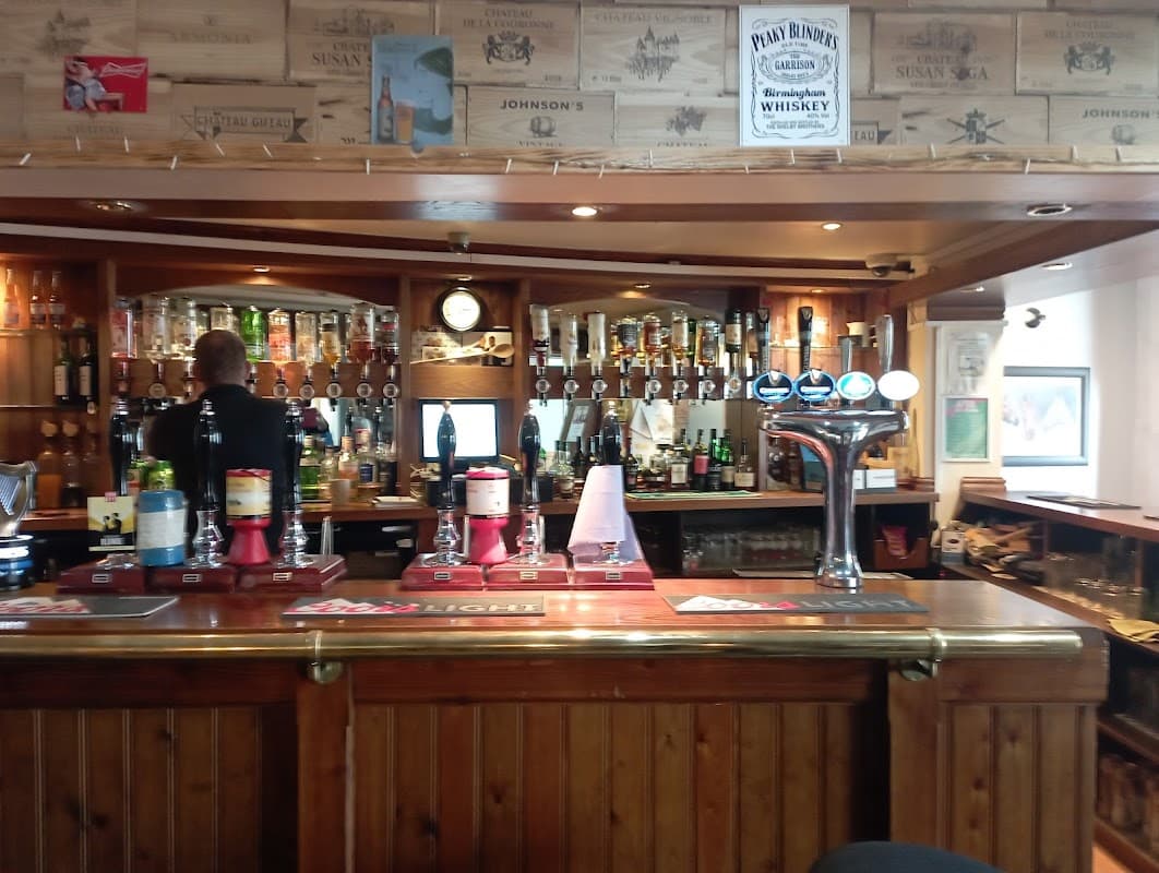 Wooden bar with various drinks, taps, and shelves of liquor; bartender serving in a cozy, rustic setting.