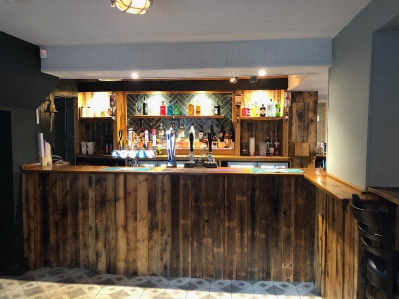 Wooden bar with a variety of drinks displayed on shelves, modern decor, and patterned floor tiles.