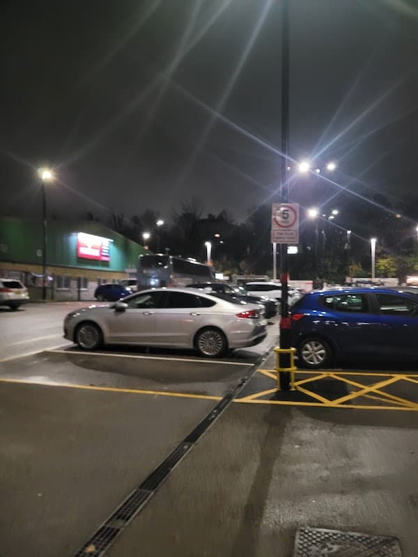 Pay & Display parking area in Brighouse, Yorkshire, with silver and blue cars under bright lights at night.