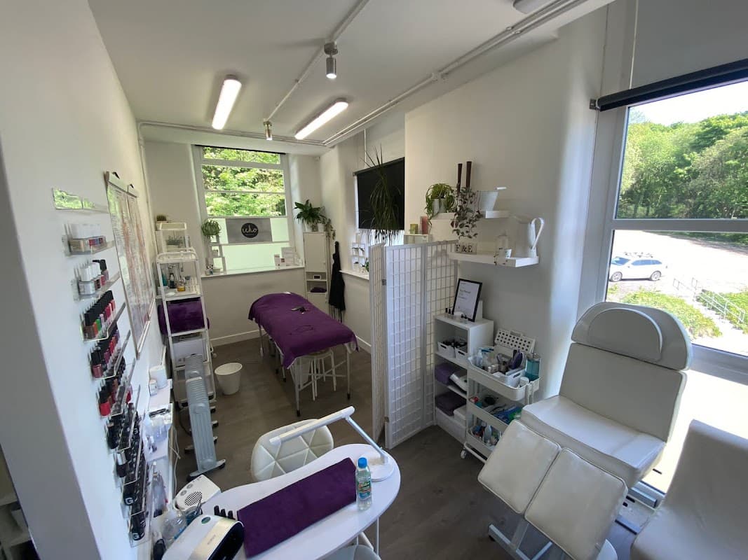 Bright beauty salon with a treatment bed, white furniture, plants, and nail polish displays in a modern setting.