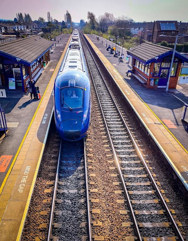 A blue train at Brough station, with platforms, tracks, and passengers waiting nearby under clear skies.