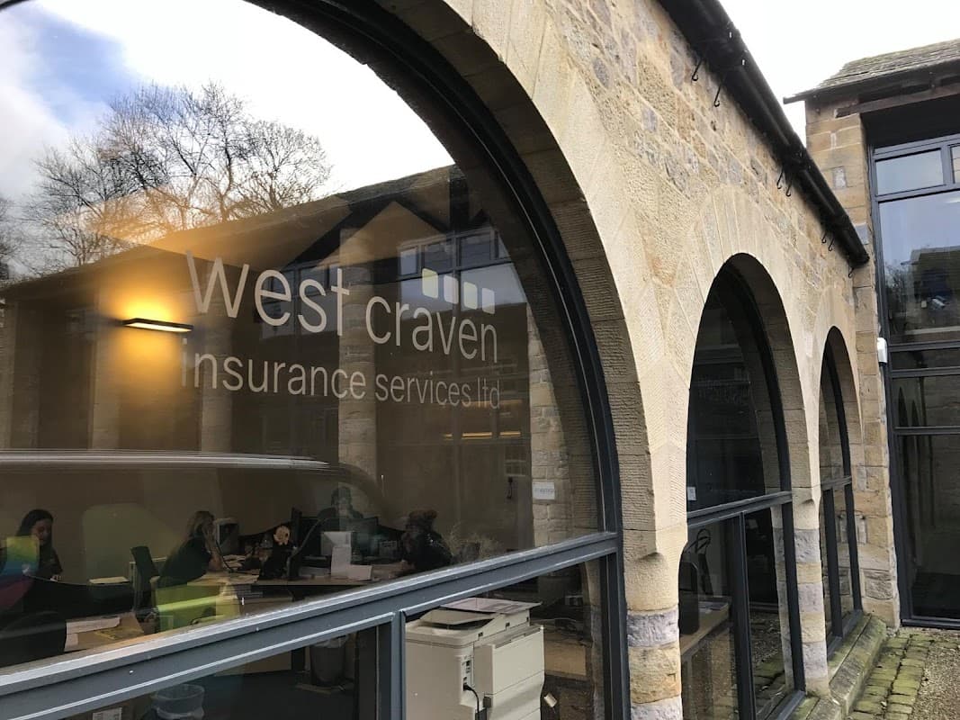 West Craven Insurance Services Ltd sign on a stone building with large arched windows, reflecting a busy office inside.