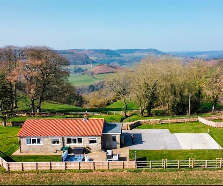 Luxury lodge with a red-tiled roof, surrounded by green fields and hills in Broxa, North Yorkshire.