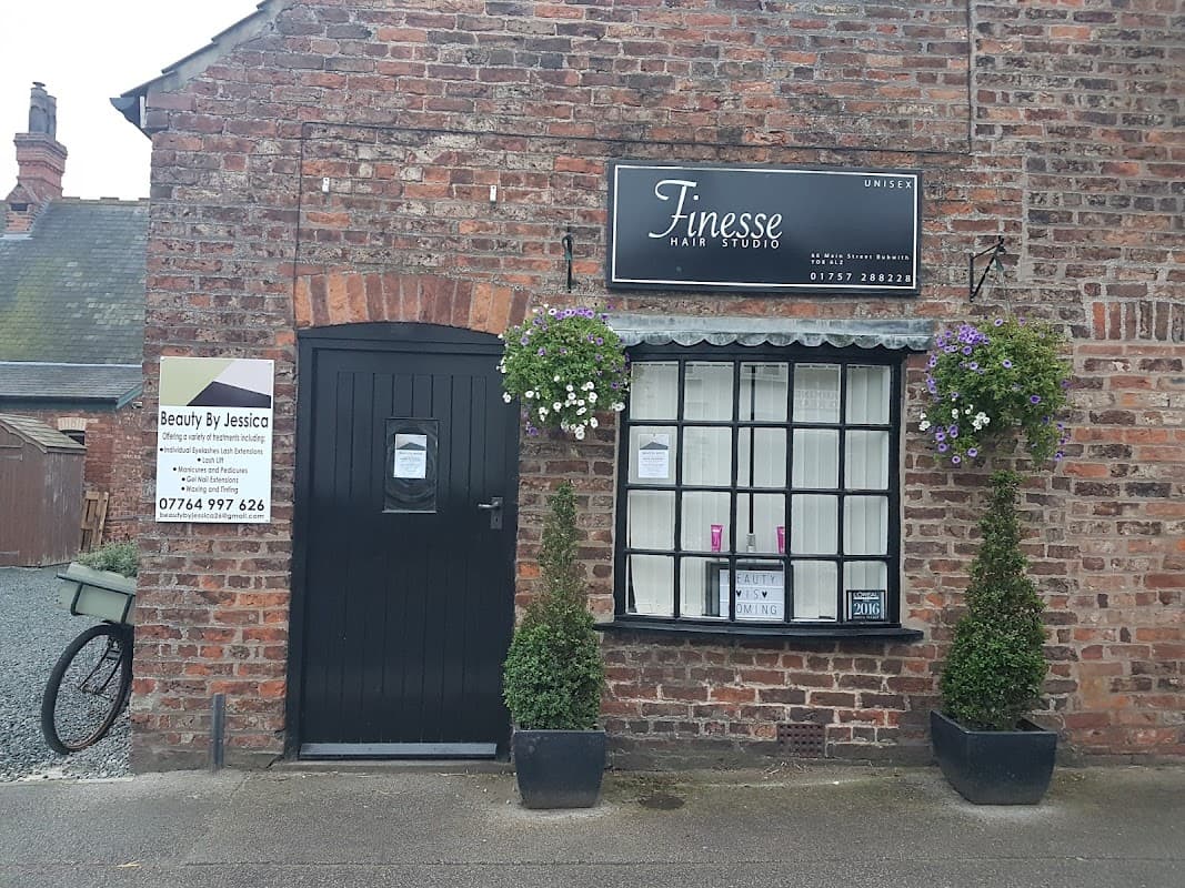Brick building with a black door, window with flower baskets, and a sign for "Finesse Hair Studio" and "Beauty By Jessica."