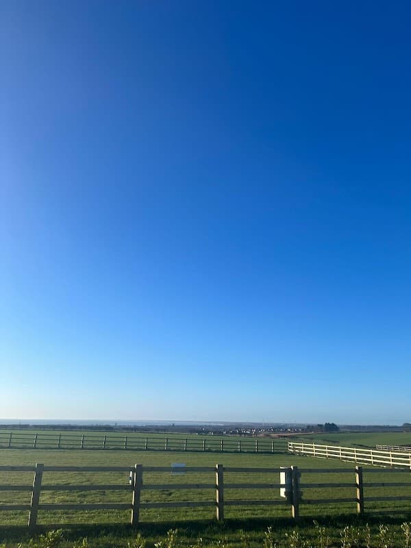 Clear blue sky over a green field with wooden fences, typical of a serene caravan park setting in Yorkshire.