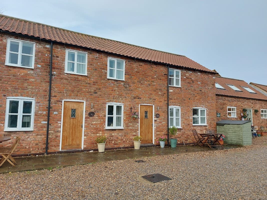 Charming brick cottages with wooden doors, potted plants, and outdoor seating in a tranquil rural setting.