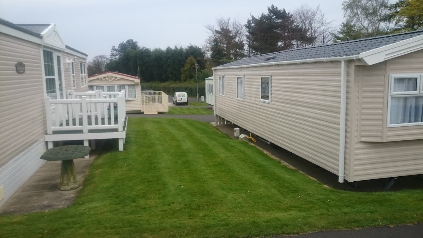 Two holiday homes with light-colored exteriors, surrounded by neatly trimmed grass and trees in the background.