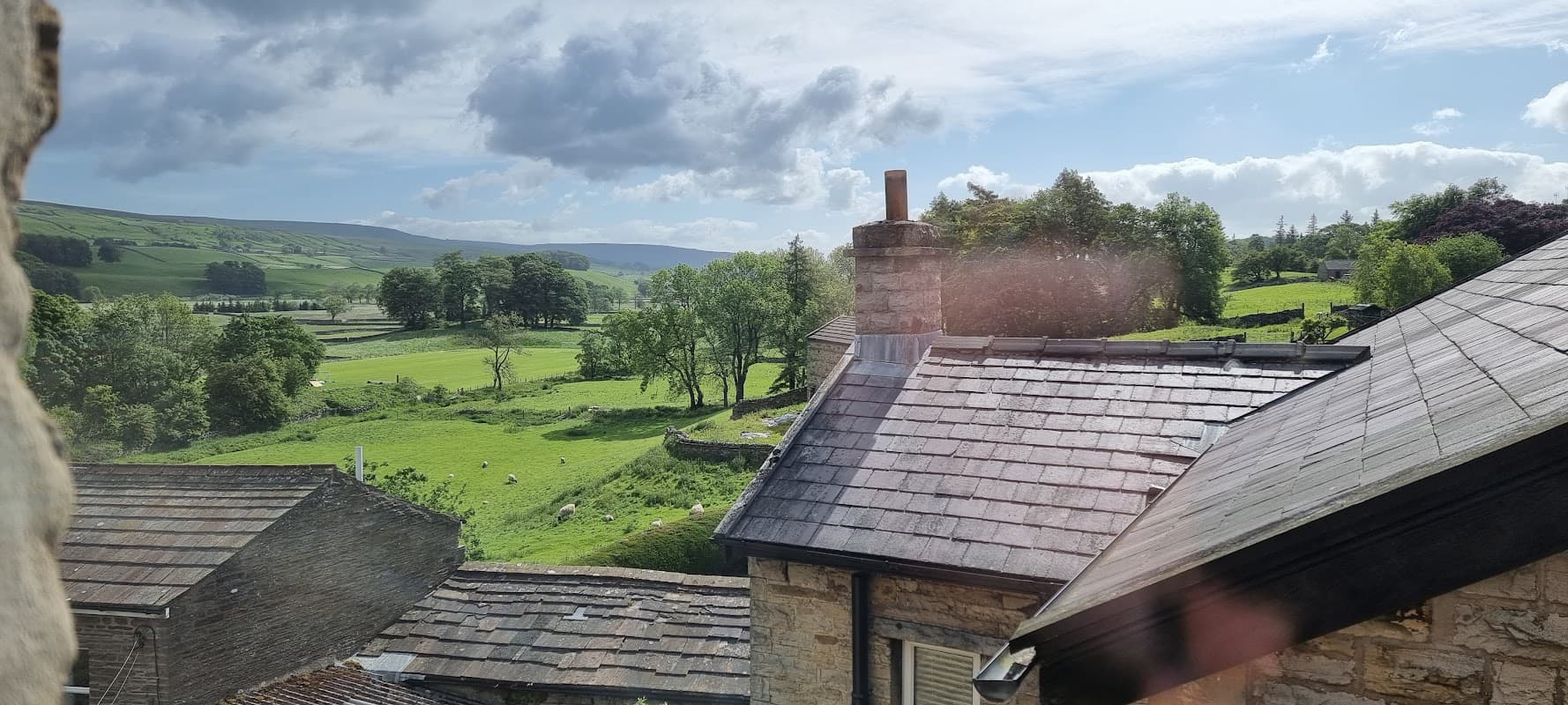 View of rolling green hills and trees from Ebor House, with a chimney and rooftops in the foreground.