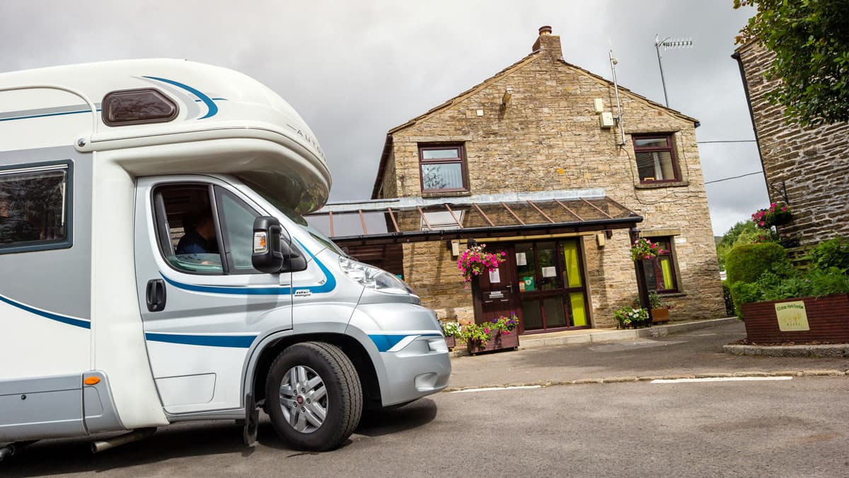 A motorhome parked in front of a stone building with flower baskets and a glass entrance in Burtersett, Yorkshire.