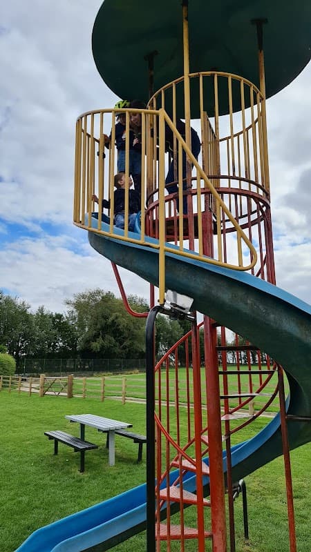 Colorful spiral slide with children playing, surrounded by green grass and trees, near Burton Pidsea Memorial Hall.