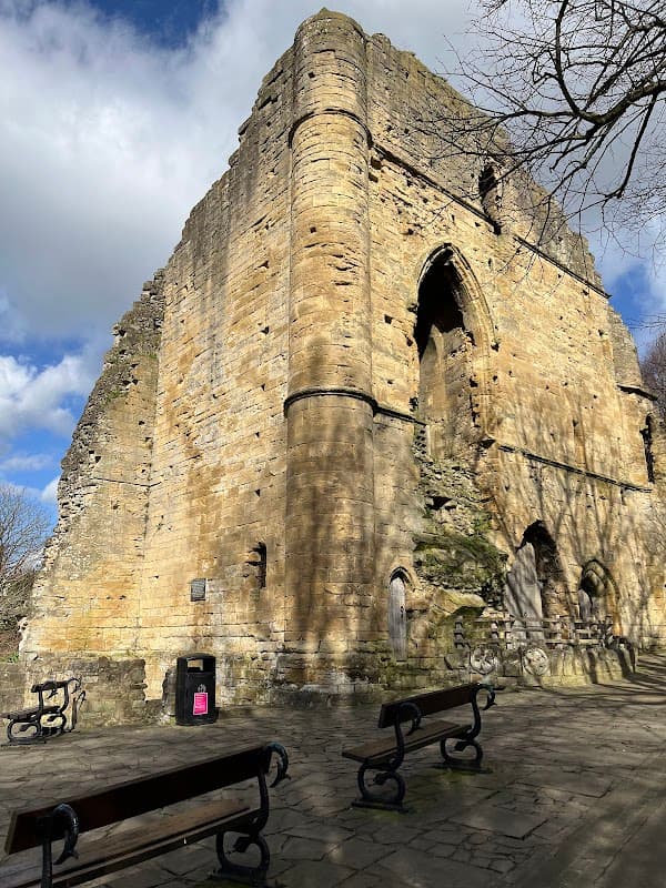 Knaresborough Castle ruins with stone walls, archway, and benches under a partly cloudy sky.
