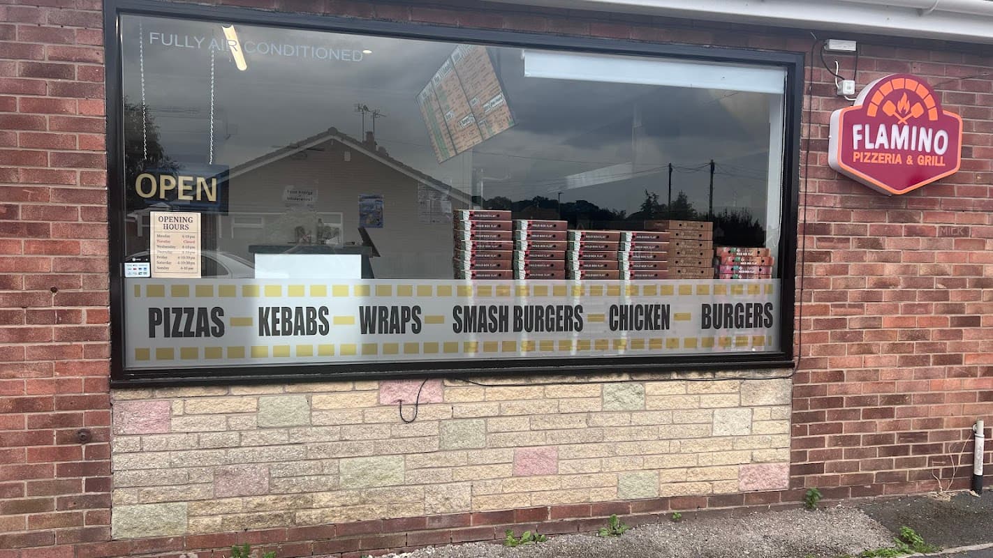 Flamino Pizzeria & Grill sign with menu items displayed in the window, featuring pizzas, kebabs, burgers, and wraps.