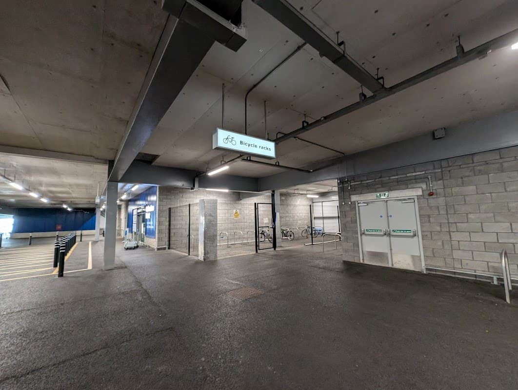 Bicycle parking area with a sign, bike racks, and a spacious concrete floor in a car park.