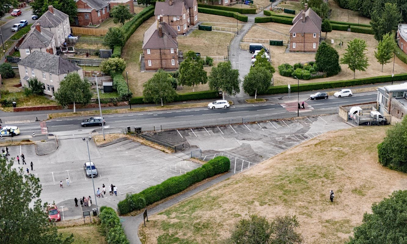 Aerial view of Firth Park Car Park with vehicles, grassy areas, and residential buildings in the background.