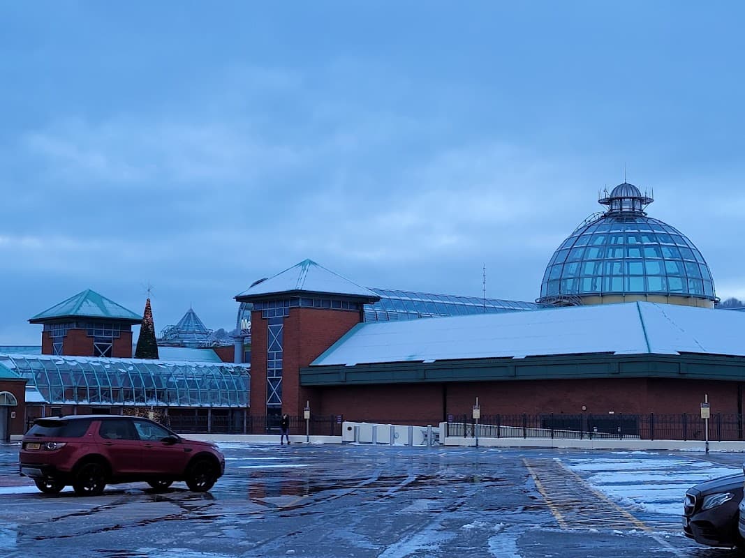 Snow-covered parking lot with a modern building featuring a glass dome and green roofs in a cloudy sky.