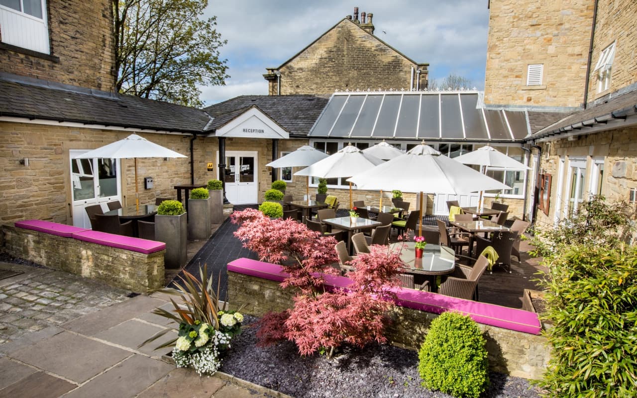 Charming outdoor seating area at Herriots Hotel, featuring umbrellas, plants, and a pink bench in a picturesque setting.
