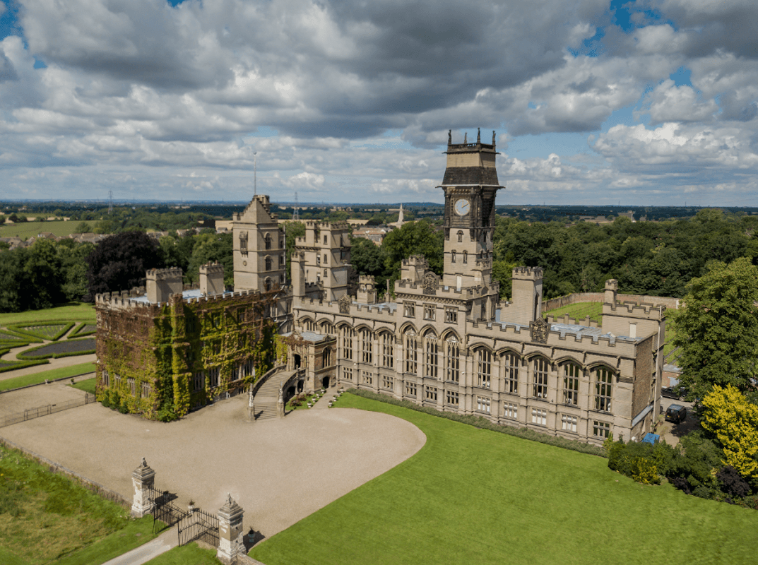 Historic Carlton Towers Estate features a grand castle with a clock tower, surrounded by lush greenery and gardens.