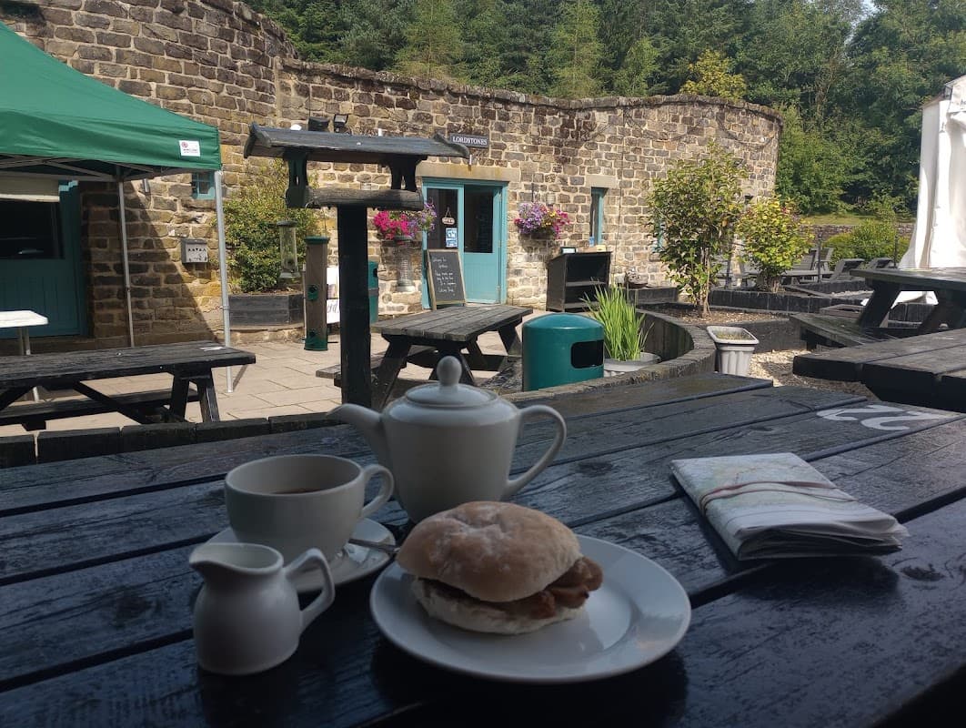 A rustic outdoor seating area with a table set for breakfast, featuring a tea set, a sandwich, and a menu.