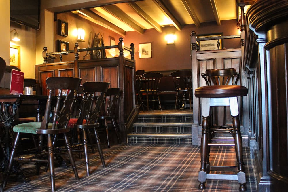 Wooden furnishings and a cozy atmosphere with a carpeted floor and warm lighting in a pub setting.