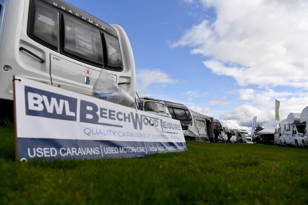 Beechwood Leisure sign in front of a row of caravans and motorhomes on a grassy area under a cloudy sky.
