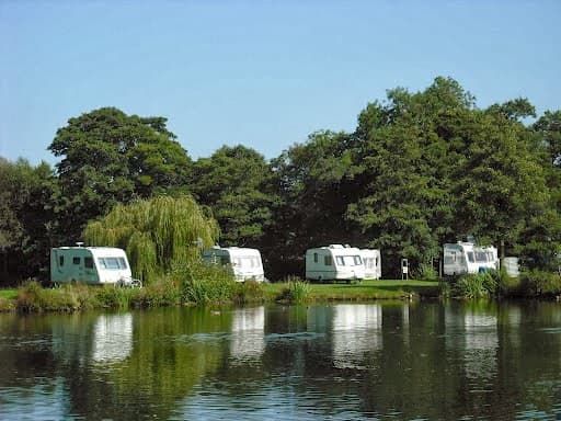 Caravans by a serene lake surrounded by lush greenery at Lakeside Caravan Park, Thirsk, Yorkshire.