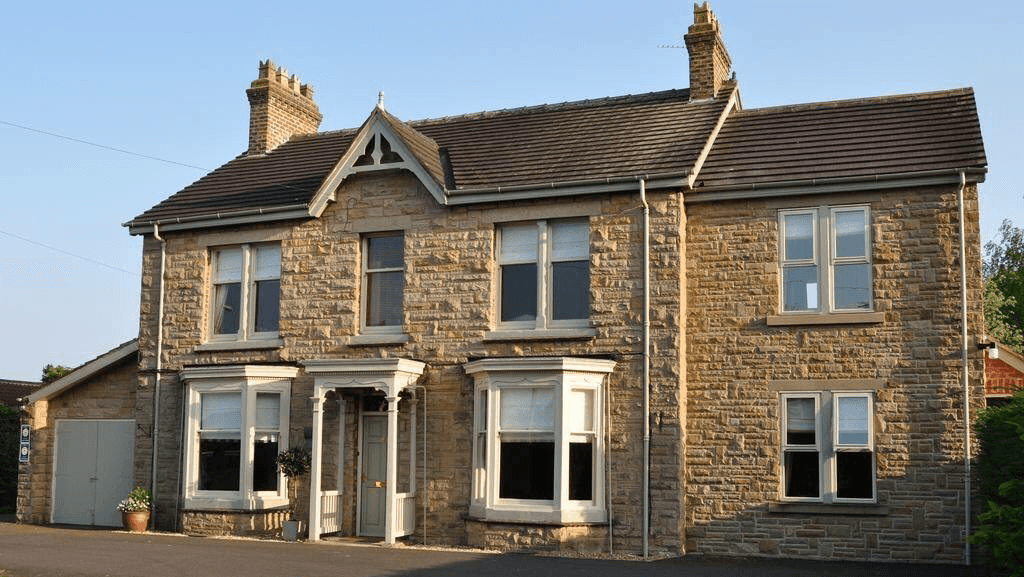 Victorian-style stone building with large windows and a welcoming entrance, surrounded by a driveway and greenery.