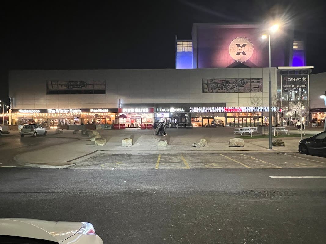 Xscape Castleford car park at night, featuring restaurants like Five Guys and Taco Bell, with bright signage and lights.