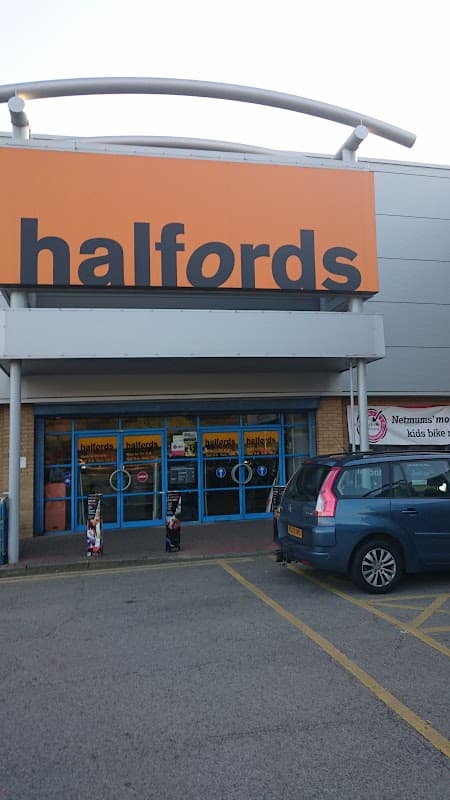 Halfords store entrance with large orange signage, blue doors, and a parked car in front.