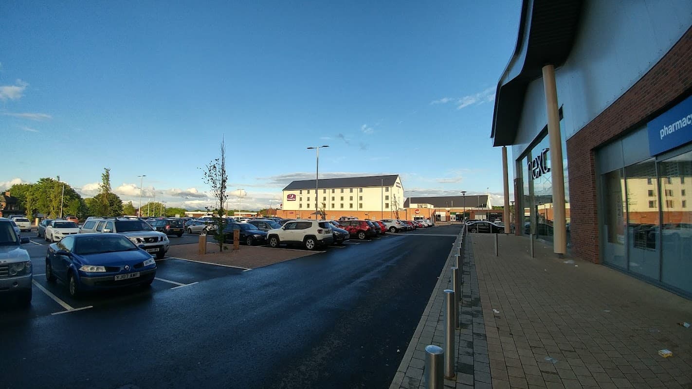 Premier Inn Catterick Garrison hotel with a parking lot and nearby retail buildings under a clear blue sky.