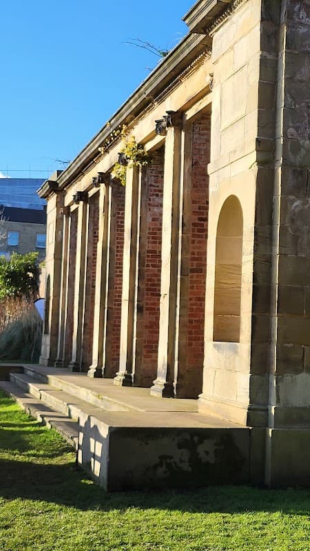 Historic stone building with columns, set in a green park under a clear blue sky.