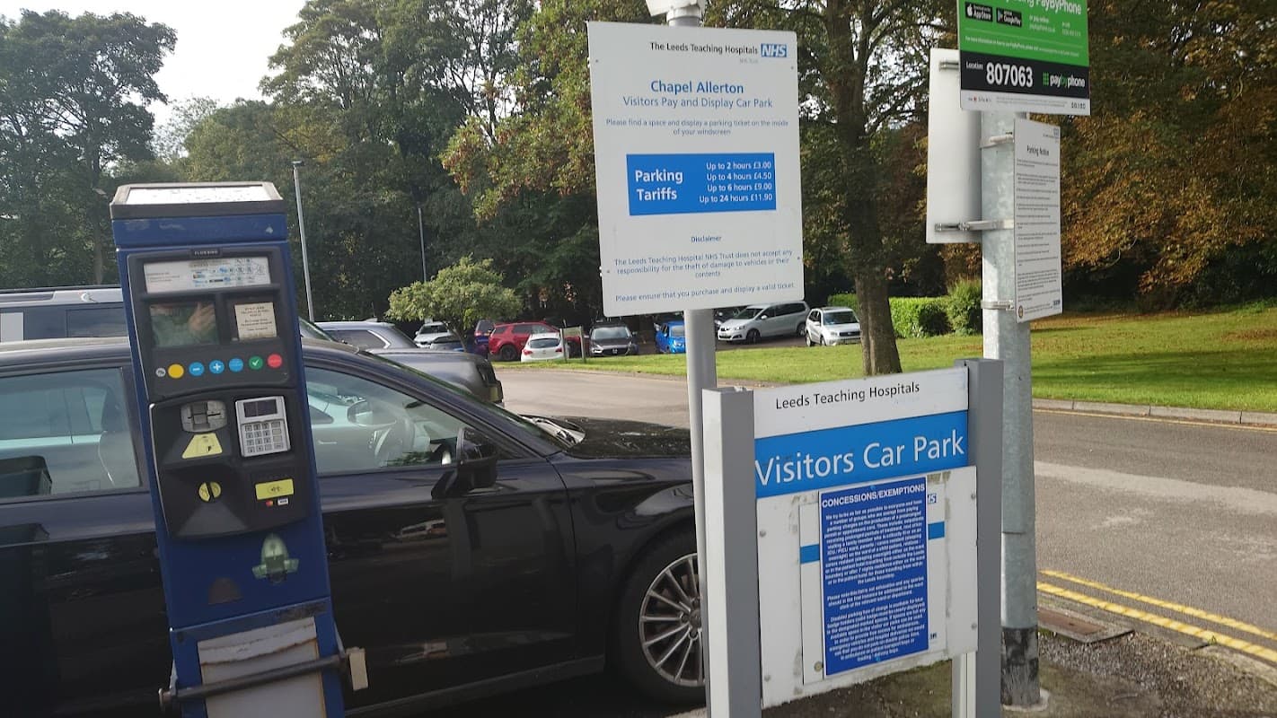 Chapel Allerton Hospital car park with payment machine, signage, and parked cars amidst green trees.