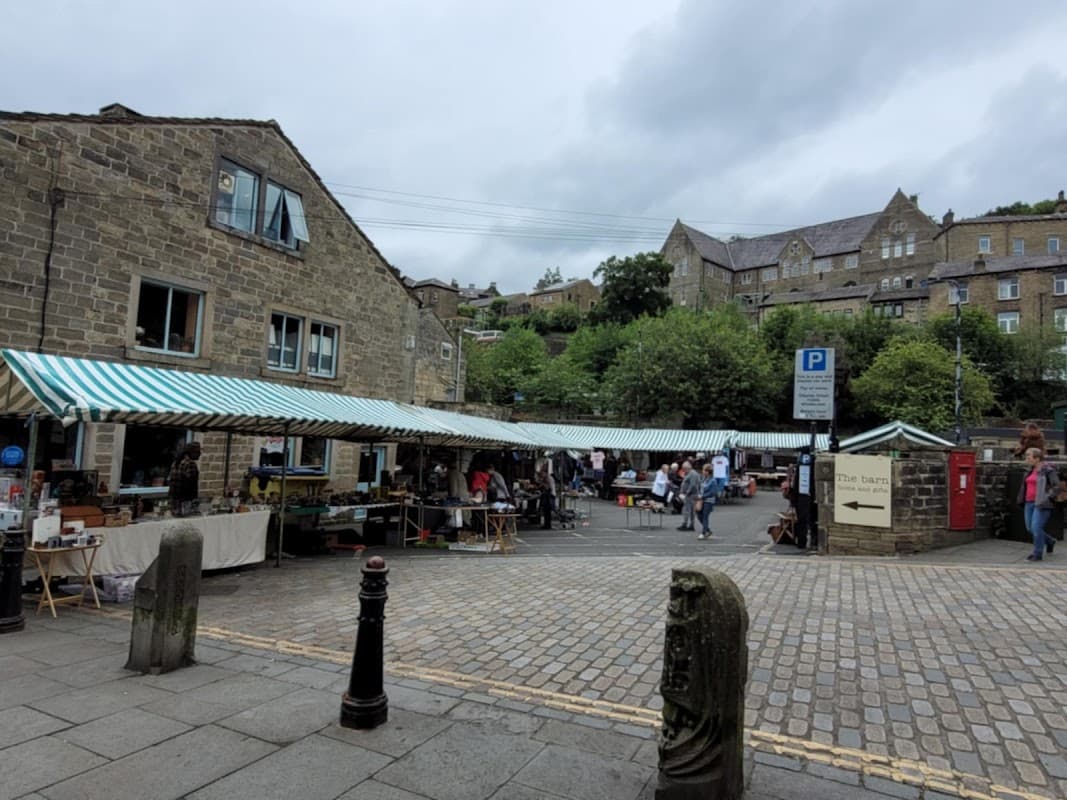 Market stalls with striped canopies line a cobblestone street, surrounded by stone buildings and greenery in Chiserley.