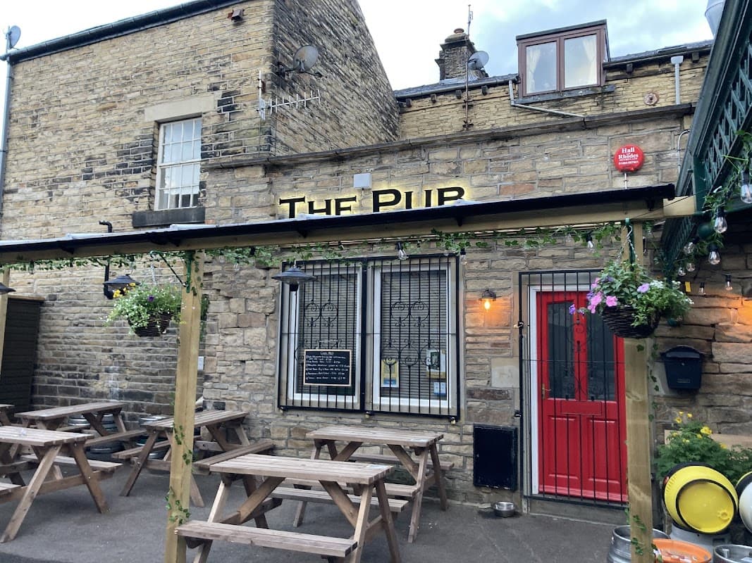 Stone exterior of a pub with a red door, outdoor seating, and hanging flower baskets in Chiserley, Yorkshire.