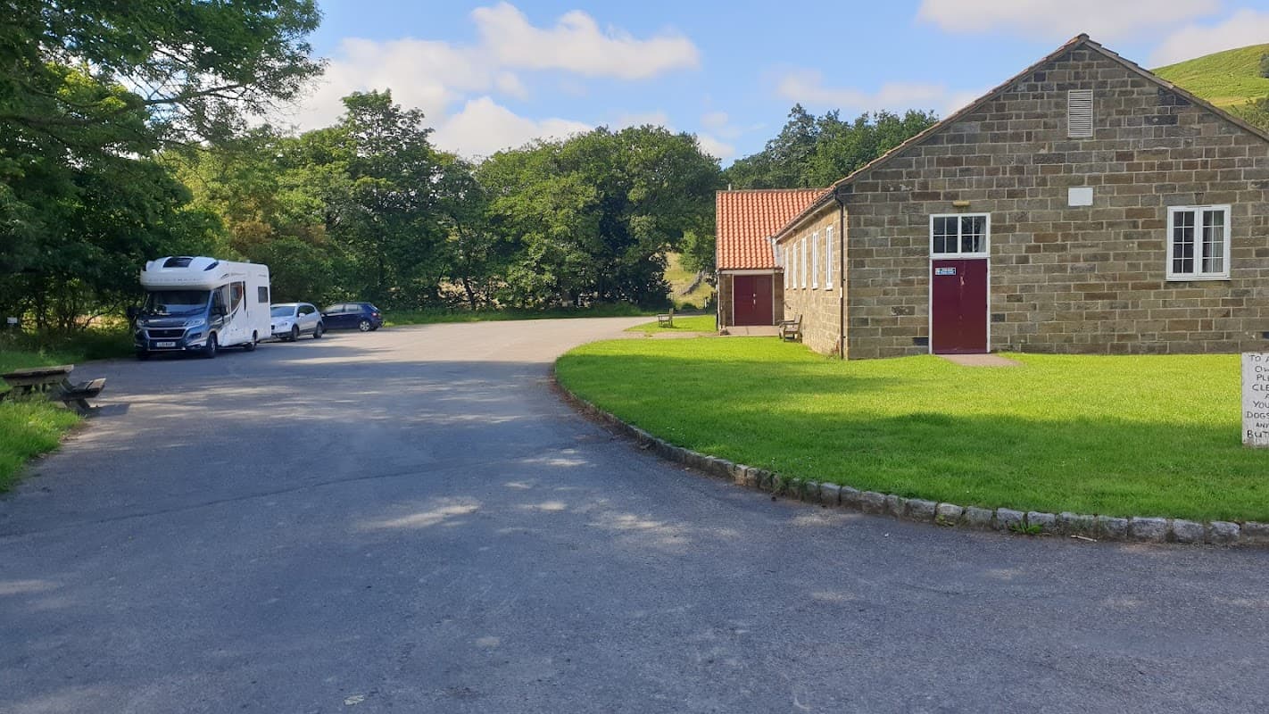 Chop Gate Village Hall with stone exterior, parked vehicles, and green landscape under a blue sky.