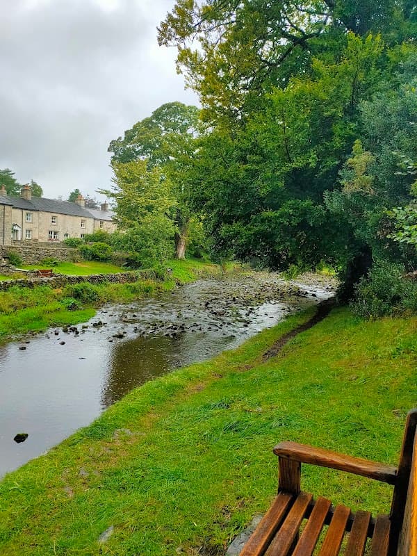 A tranquil scene by a stream, with lush greenery and a wooden bench overlooking the water near Clapham Village Hall.