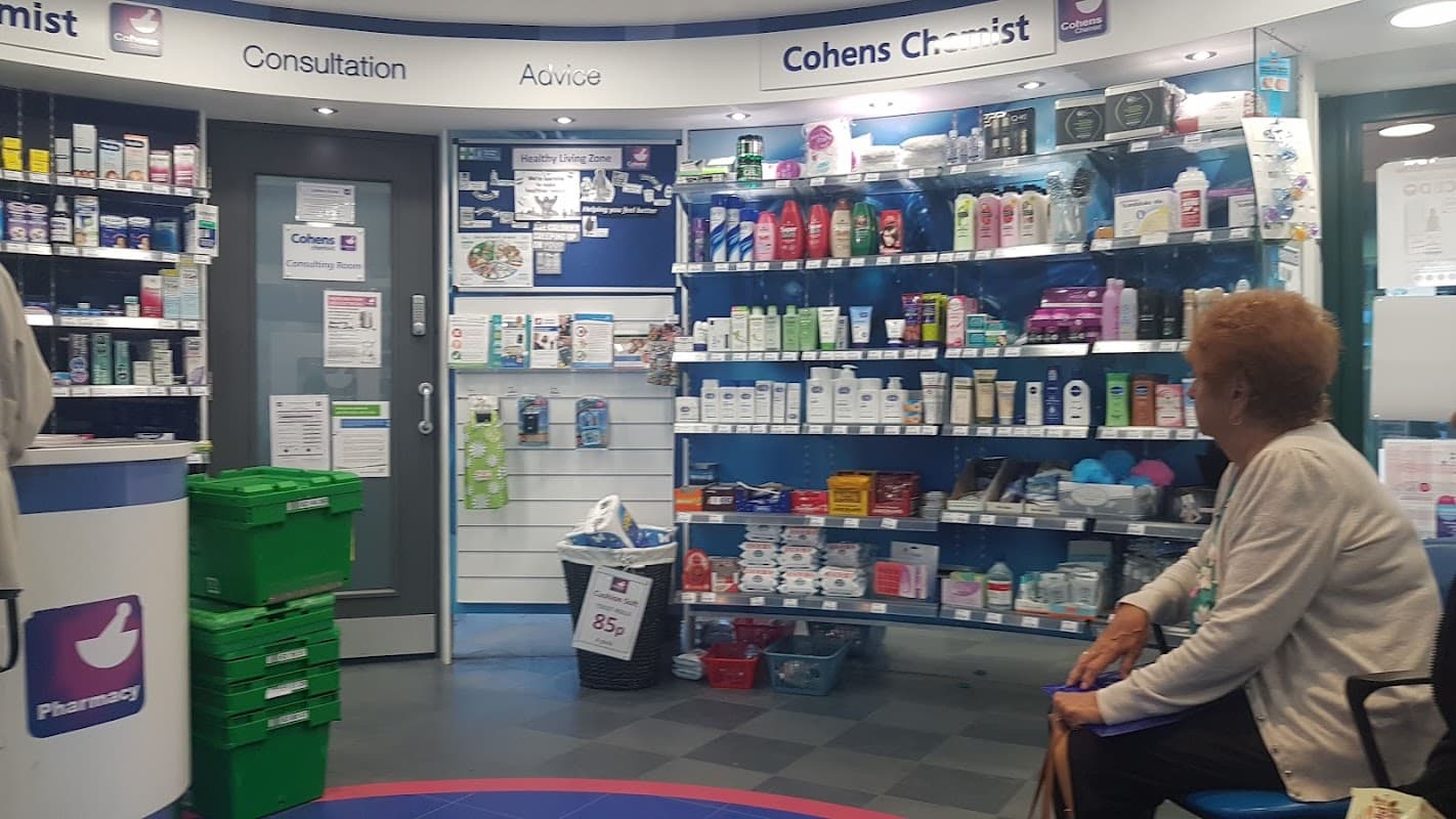 Interior of a pharmacy with shelves stocked with health products, a waiting area, and a seated elderly woman.
