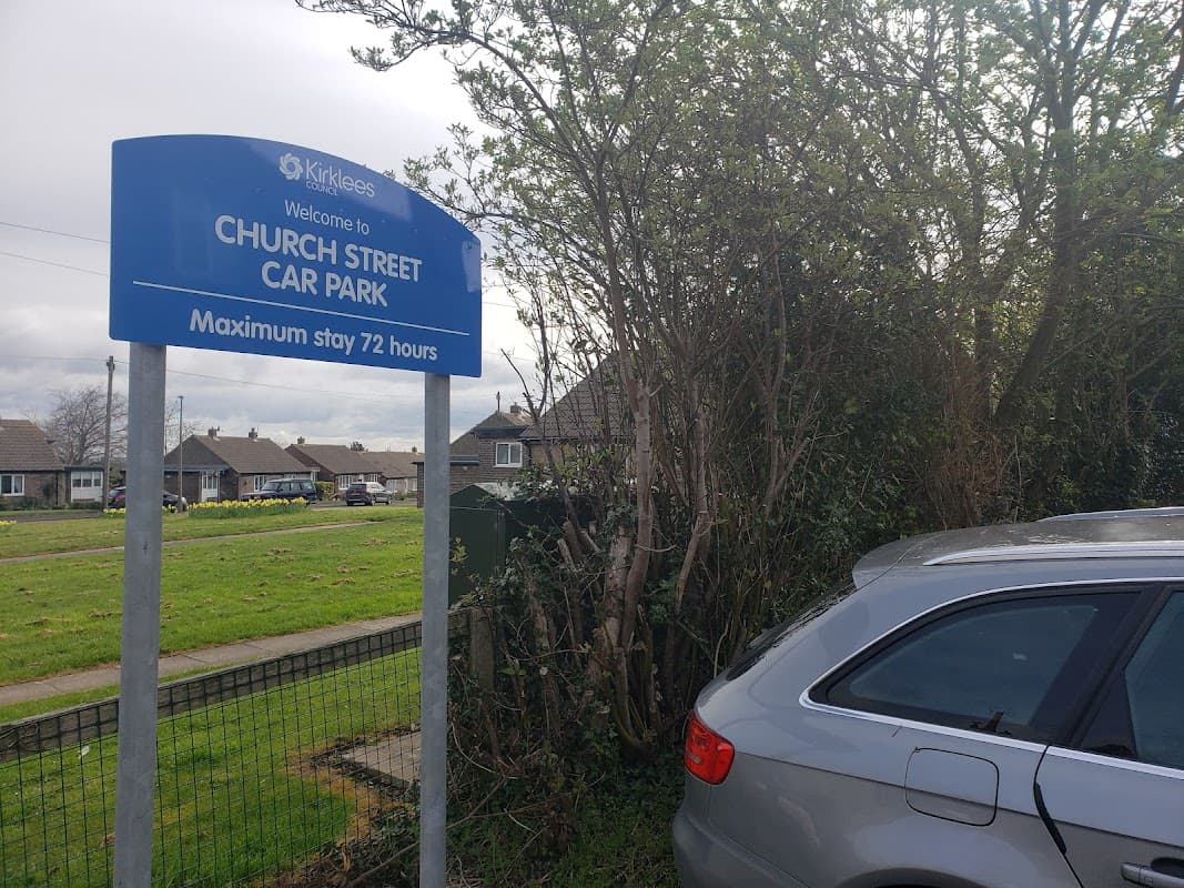 Sign for Church Street Car Park in Clayton West, with a silver car parked nearby and houses visible in the background.