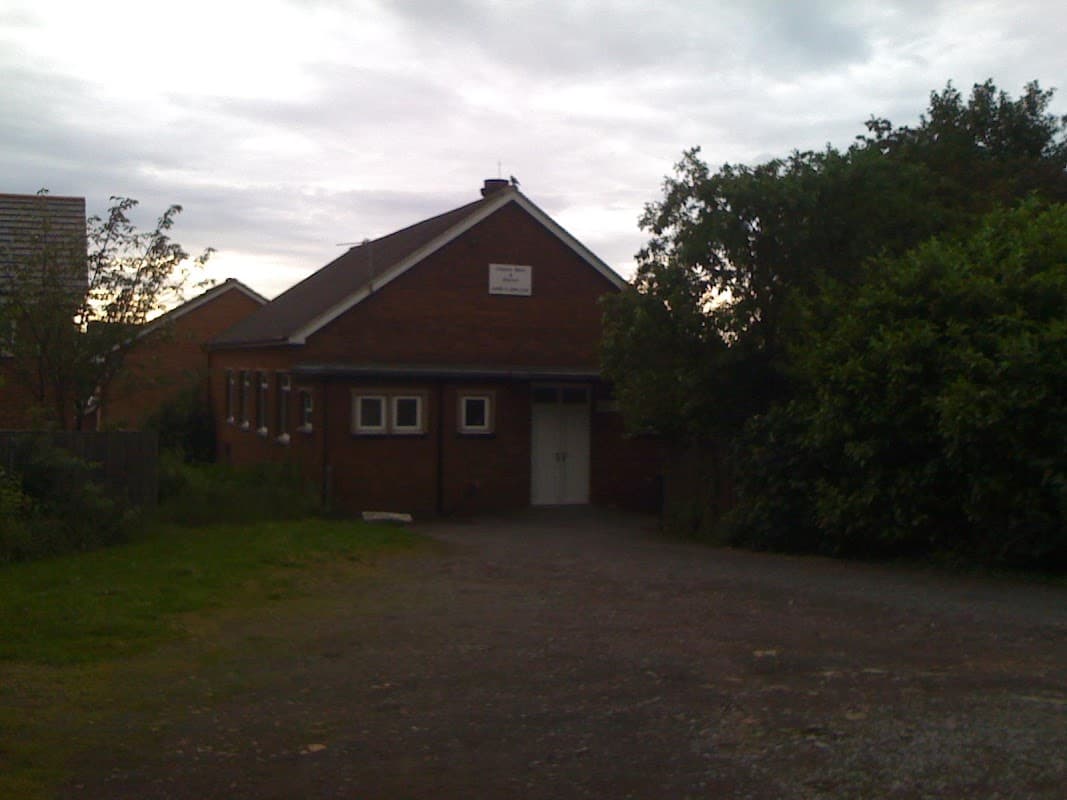 Brick building with a sign reading "Darby & Joan Club," surrounded by greenery and a gravel pathway.