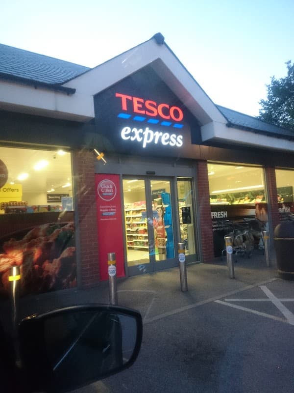 Tesco Express storefront with bright signage, shopping carts outside, and visible grocery displays inside.