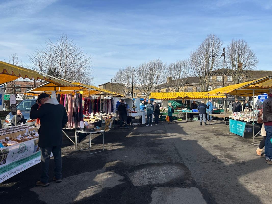 Stalls with colorful canopies displaying goods in a bustling car park, surrounded by bare trees and clear blue skies.