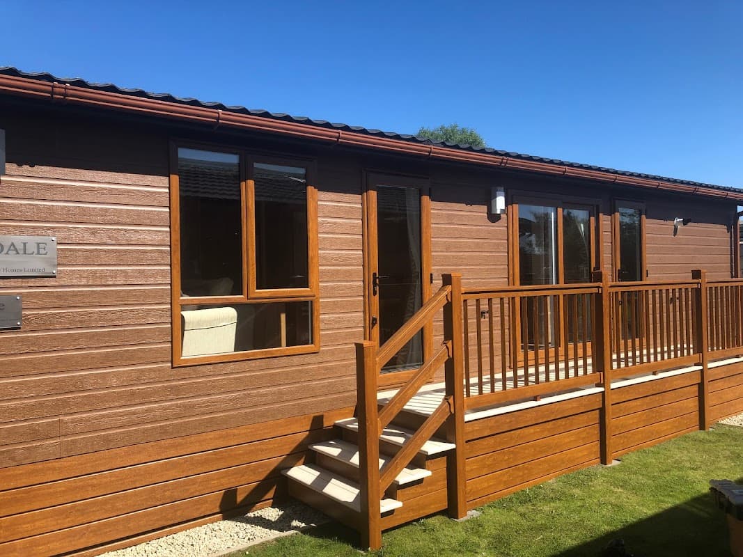 Wooden lodge with a patio and steps, set against a clear blue sky and green grass in Cliffe Common, Yorkshire.