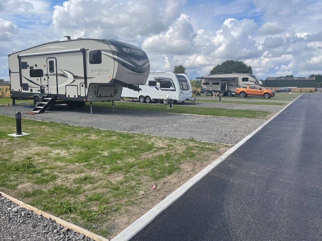 Campers parked on gravel at LINDA'S FARM, surrounded by green grass and cloudy skies in Cliffe Common, Yorkshire.