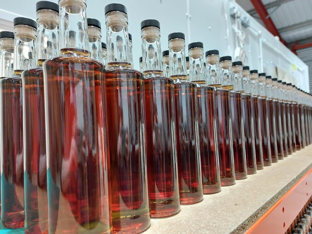 Rows of glass bottles filled with amber liquid, lined up on a shelf in a distillery setting.