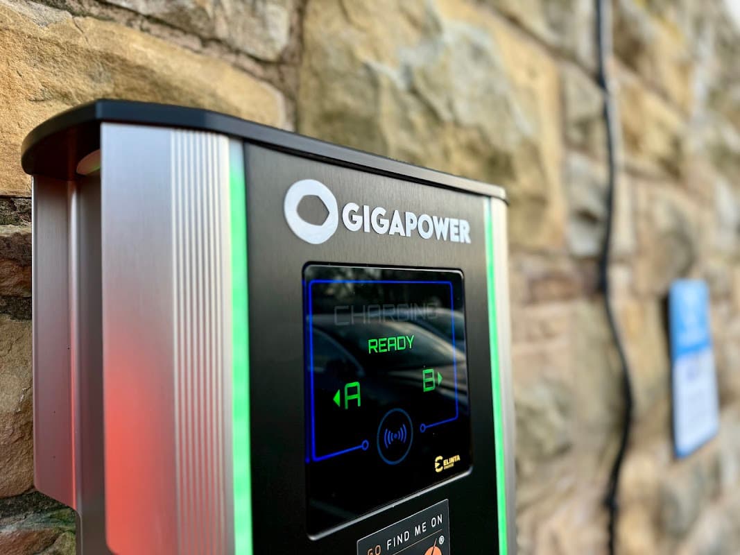 Giga Power Charging Station with illuminated display showing "READY" and options A and B, set against a stone wall.