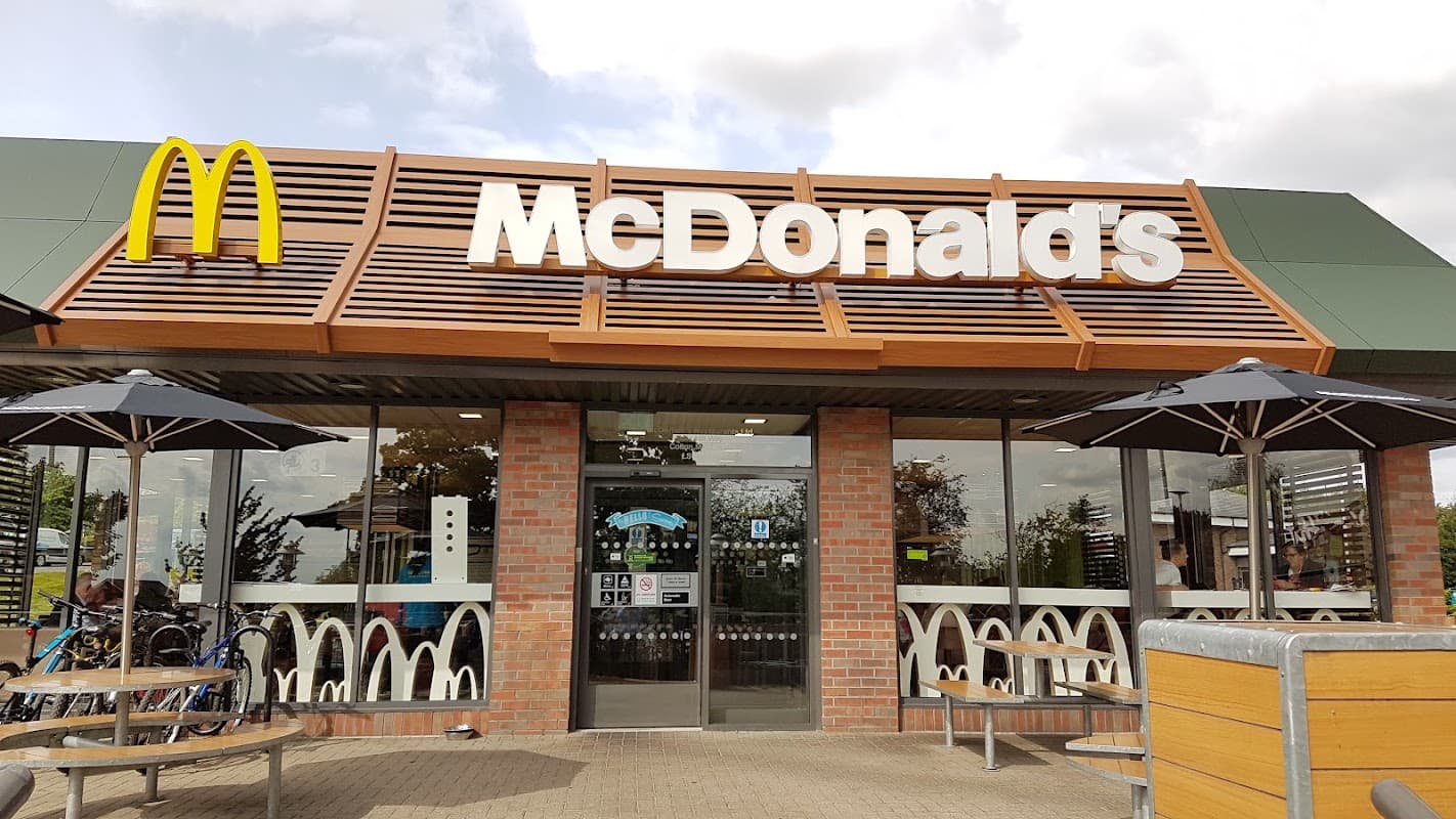 McDonald's restaurant exterior with iconic golden arches, outdoor seating, umbrellas, and bike racks in Colton, Yorkshire.