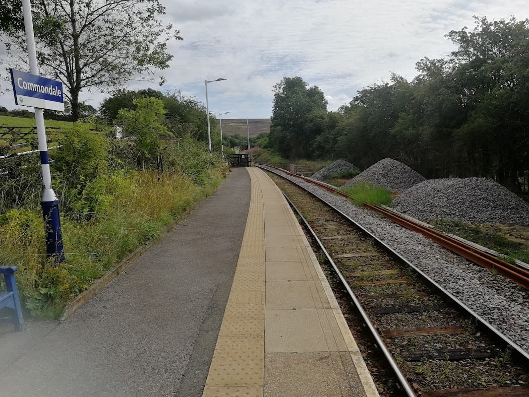 Platform at Commondale station with railway tracks, greenery, and piles of gravel under a cloudy sky.