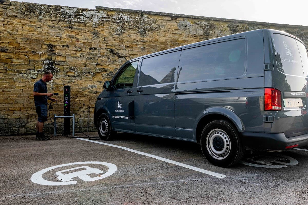 Electric vehicle charging station with a gray van parked beside it in Coneysthorpe, Yorkshire, against a stone wall.